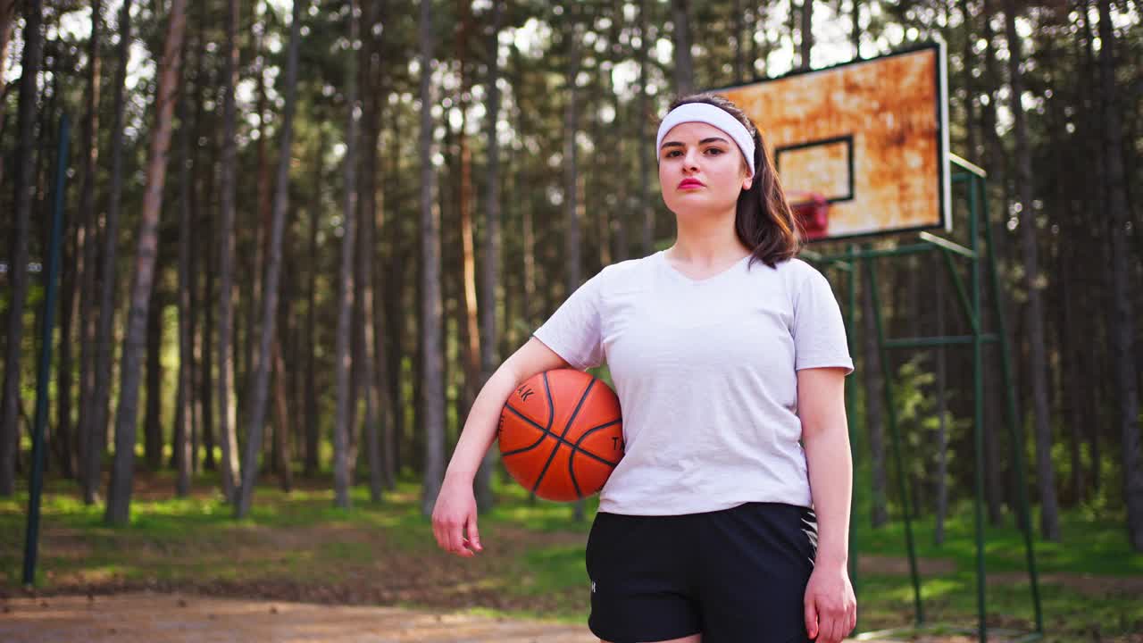 一名年轻女子手持篮球，在运动场上严肃地看着镜头视频下载