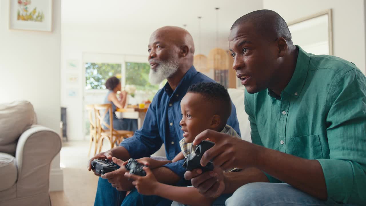 祖父与父亲和孙子在家里玩电脑游戏，背景是家人视频下载