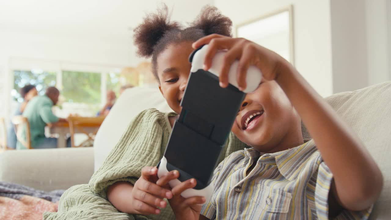 男孩和女孩在家里玩手持游戏设备，背景是多代家庭视频下载