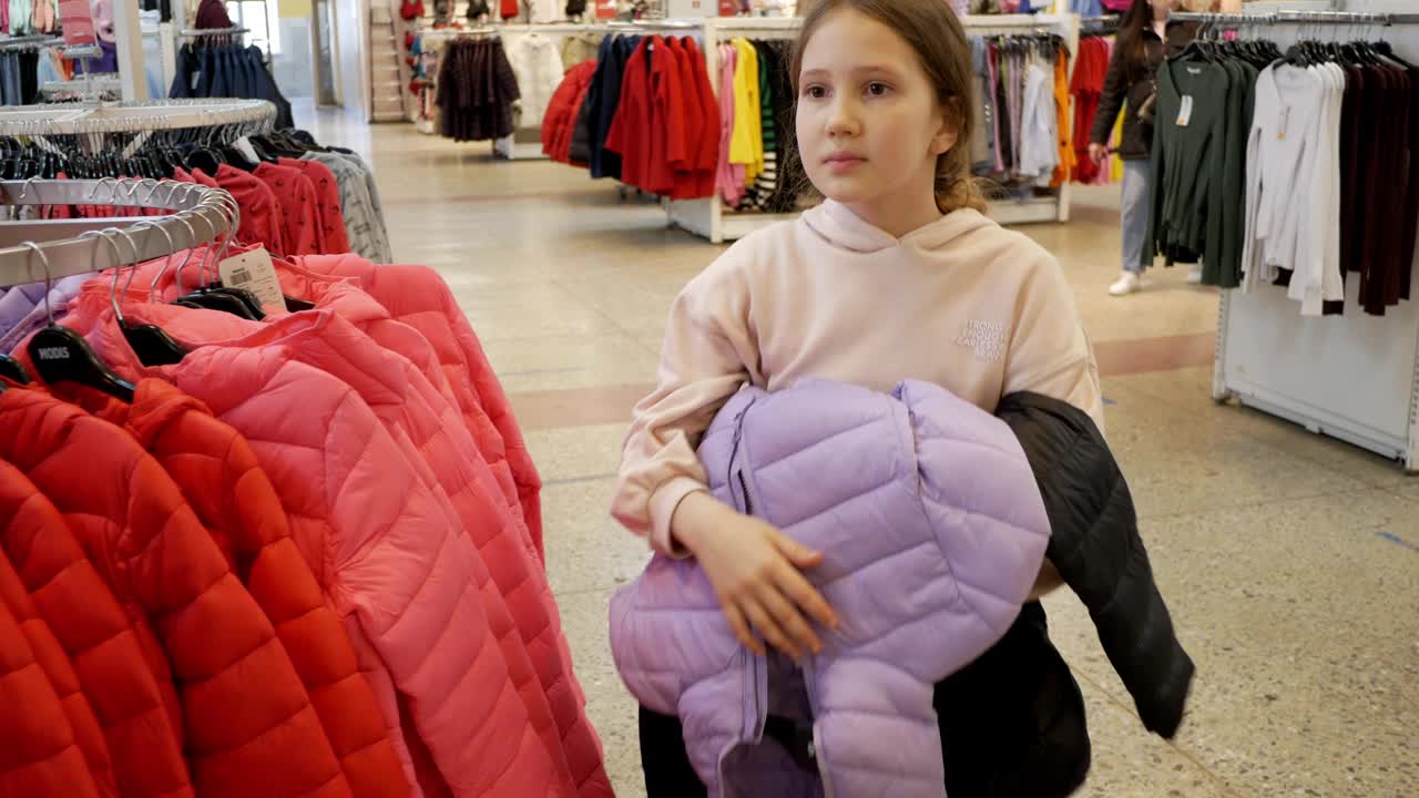 美丽微笑的少女顾客在服装店选购时髦的衣服——夹克和双肩包。女孩在时尚的商店，可持续的品牌设计，新系列。特写镜头视频下载