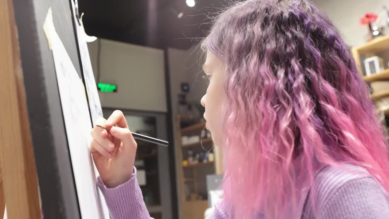 可爱的粉色头发的女孩在画布上画画，拿着铅笔，享受创作的爱好，童年，训练艺术技能。视频下载