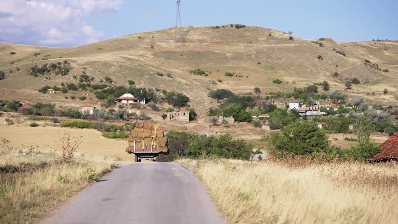 拖拉机行驶在乡村公路上，在田野上运送稻草堆、干草包，慢镜头视频下载