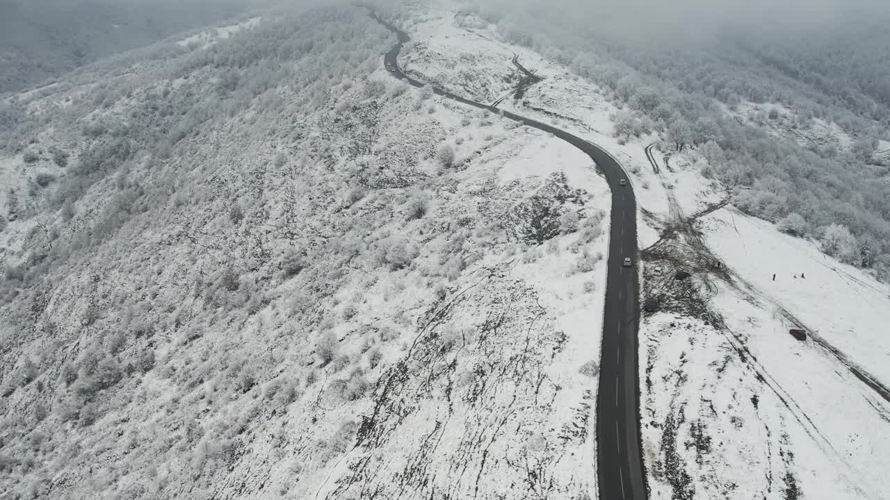 鸟瞰一群汽车行驶在湿滑的雪和蜿蜒的山路上视频下载