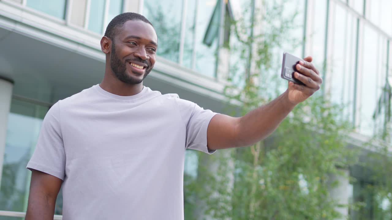 非洲裔美国人拿着智能手机在城市街道上视频聊天。男博主聊天与最好的朋友在社交网络。男子在户外进行虚拟会议在线聊天视频通话。视频下载