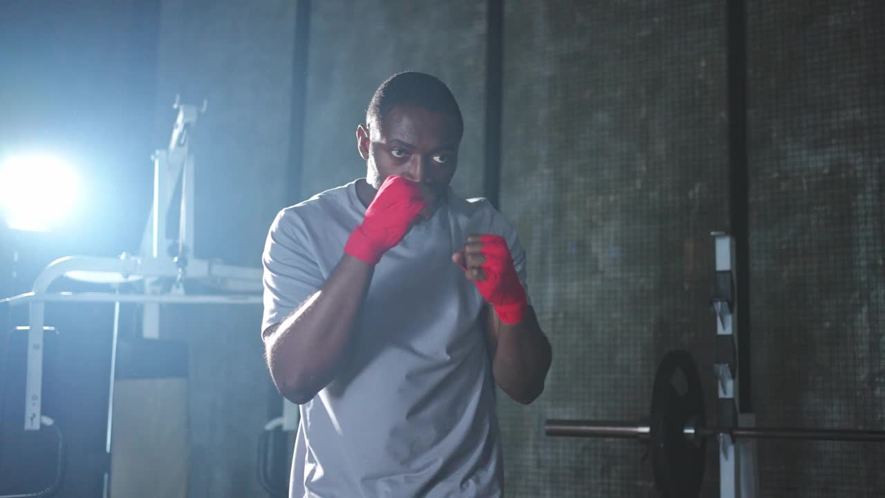 健身房里的健身训练。非洲男子拳击手在健身房用红色拳击包裹运动保护绷带，为拳击陪练训练做准备。视频下载
