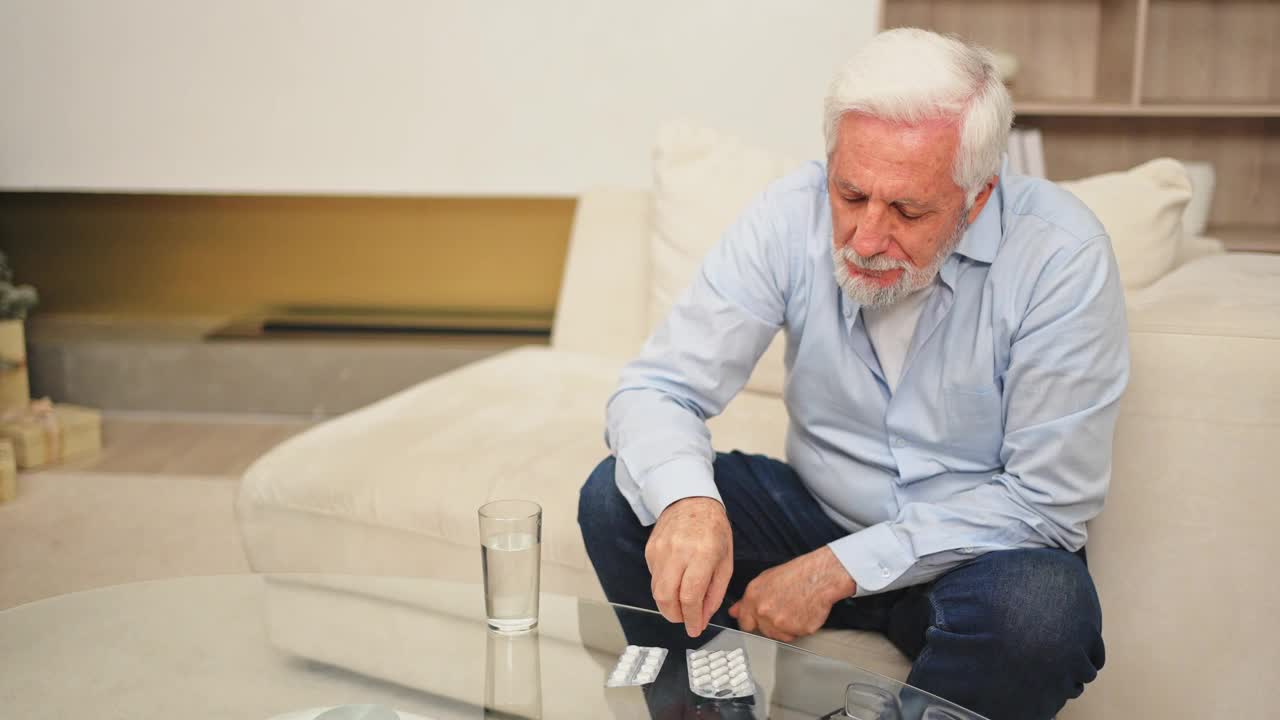中年老人拿着药片和一杯水。年事已高的老爷爷服用维他命丸治病。年龄处方药物保健治疗理念。视频下载