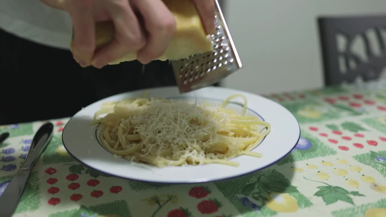 在一盘意大利面上磨碎帕玛森奶酪。视频下载