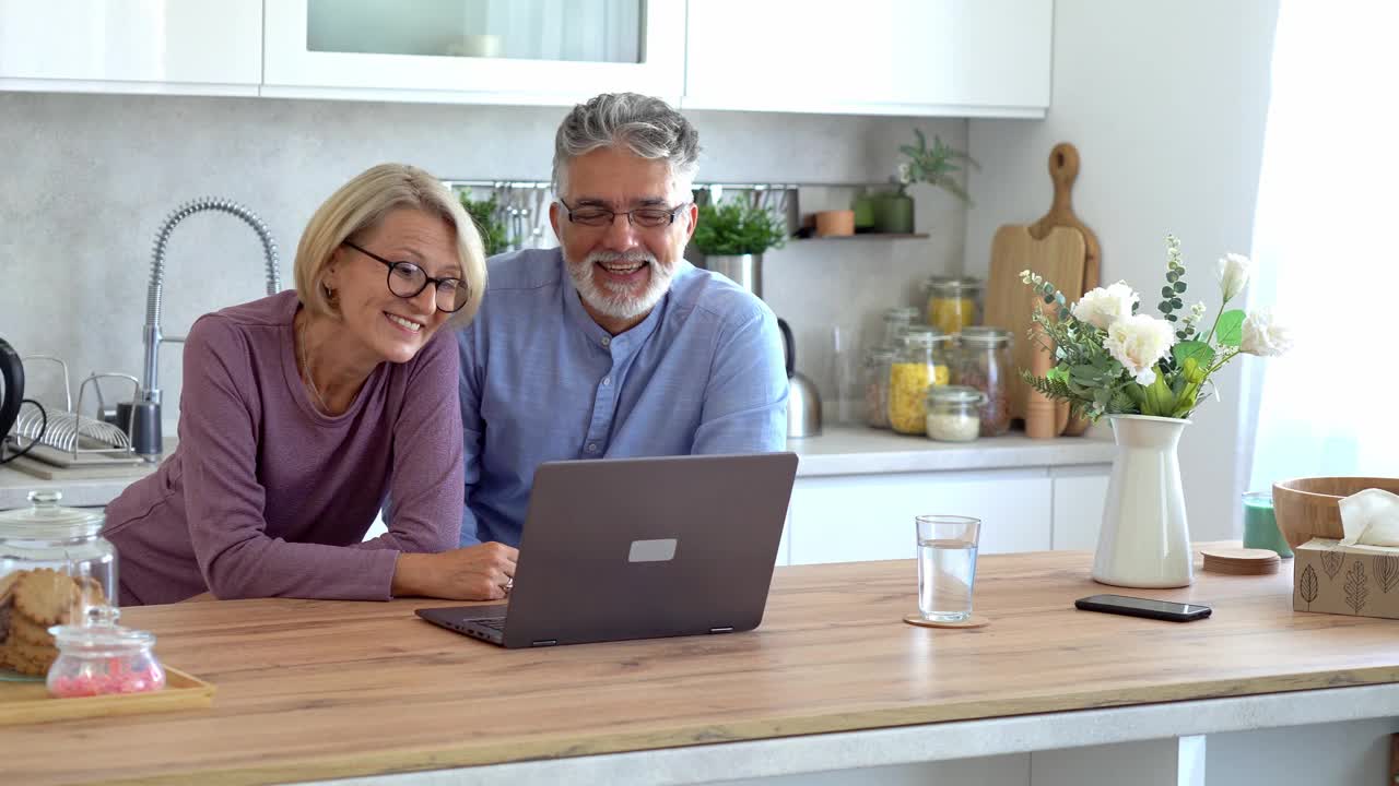 一对老夫妇在厨房里用笔记本电脑与家人在线聊天视频下载
