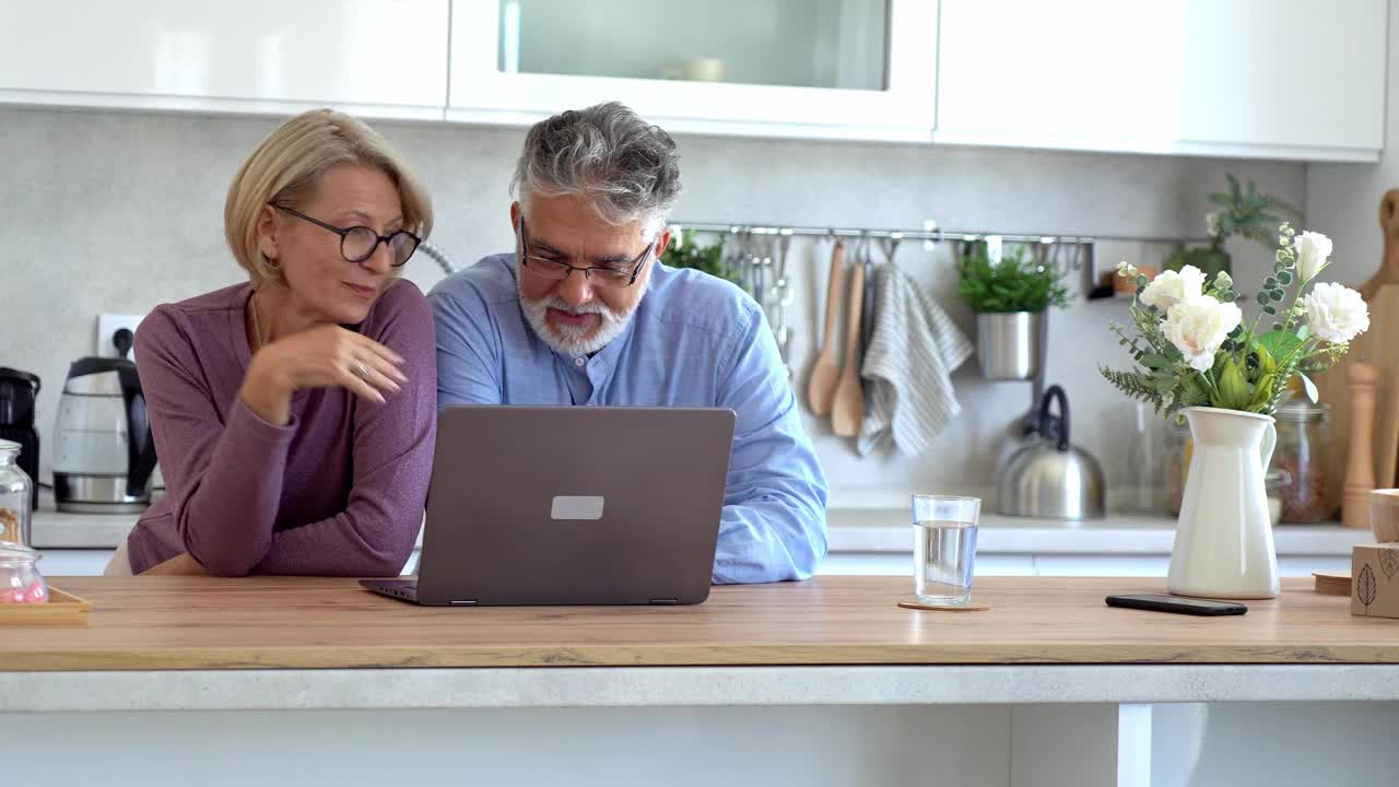 一对老年夫妇通过放在厨房柜台上的笔记本电脑参加在线会议视频下载