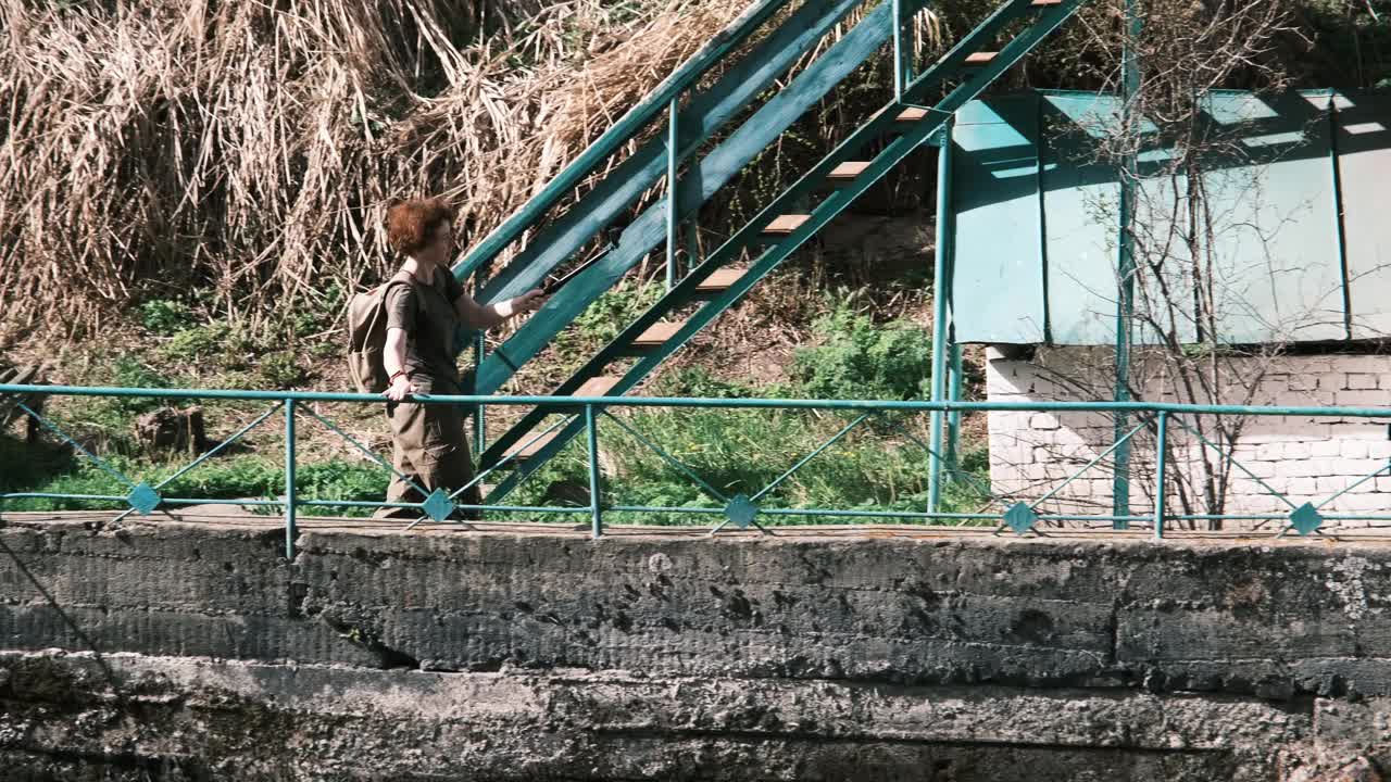 一个成熟的女人正在用动作相机拍摄山河上废弃的旧旅馆视频下载