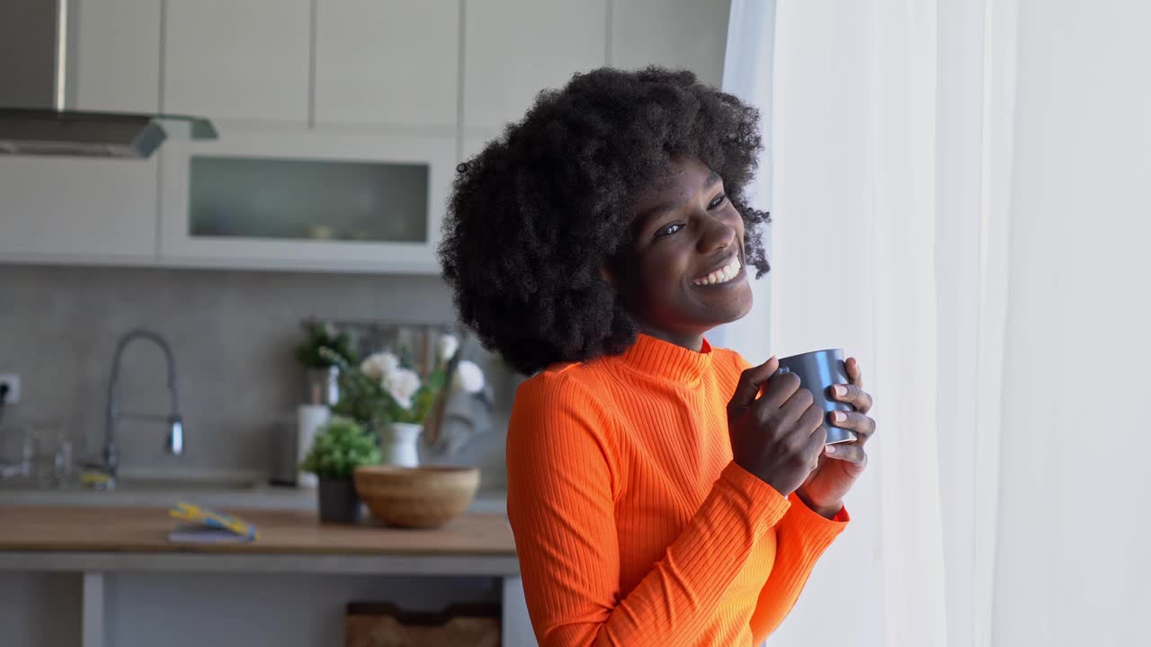 一个面带微笑的非洲妇女端着一杯咖啡望着窗外视频素材