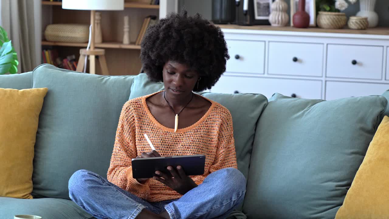 一位年轻的非裔美国女性在沙发上放松地玩着平板电脑视频素材