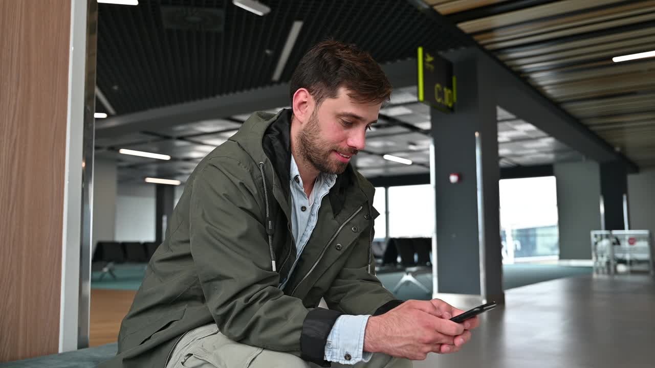 千禧一代商务旅客在机场，一边使用智能手机一边等待航班视频下载