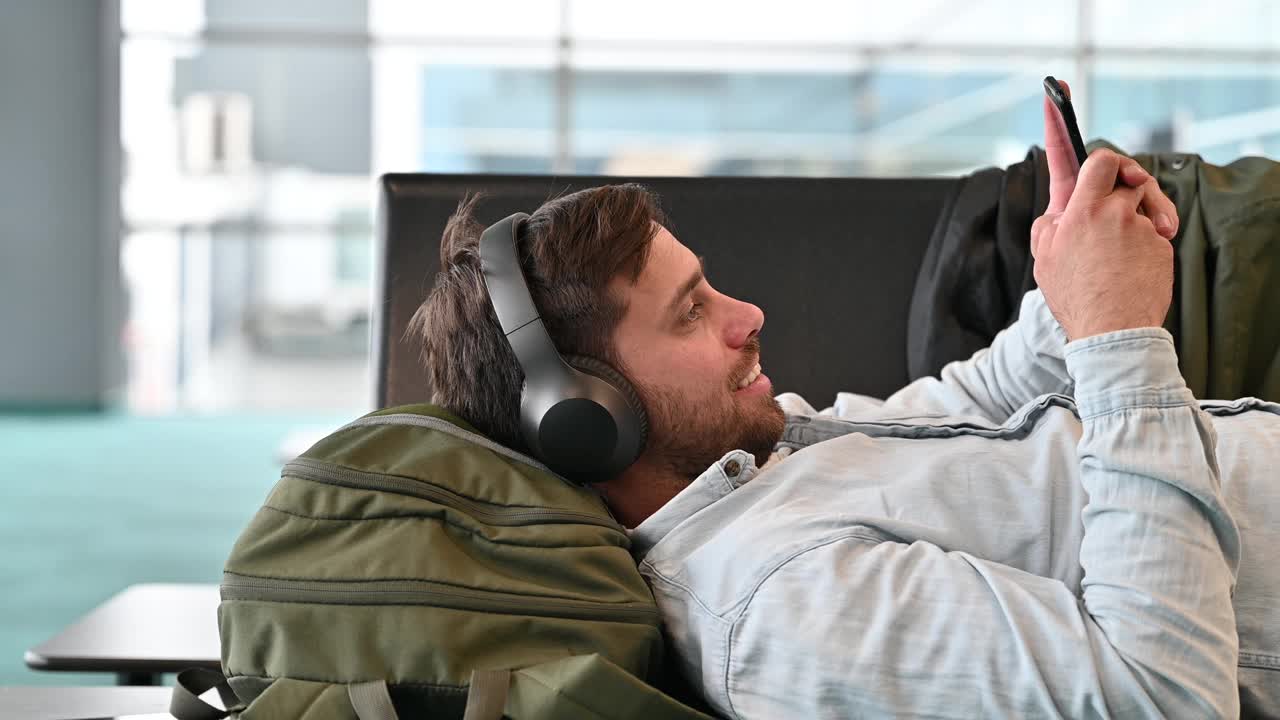 千禧一代商务旅客在机场躺着等待时使用智能手机和互联网数据视频下载