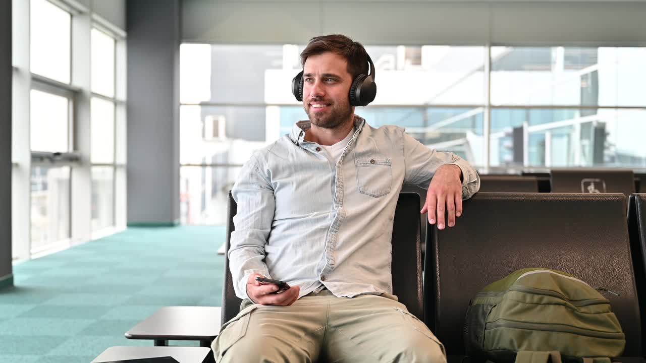 千禧一代商务旅客在机场使用智能手机和耳机视频下载