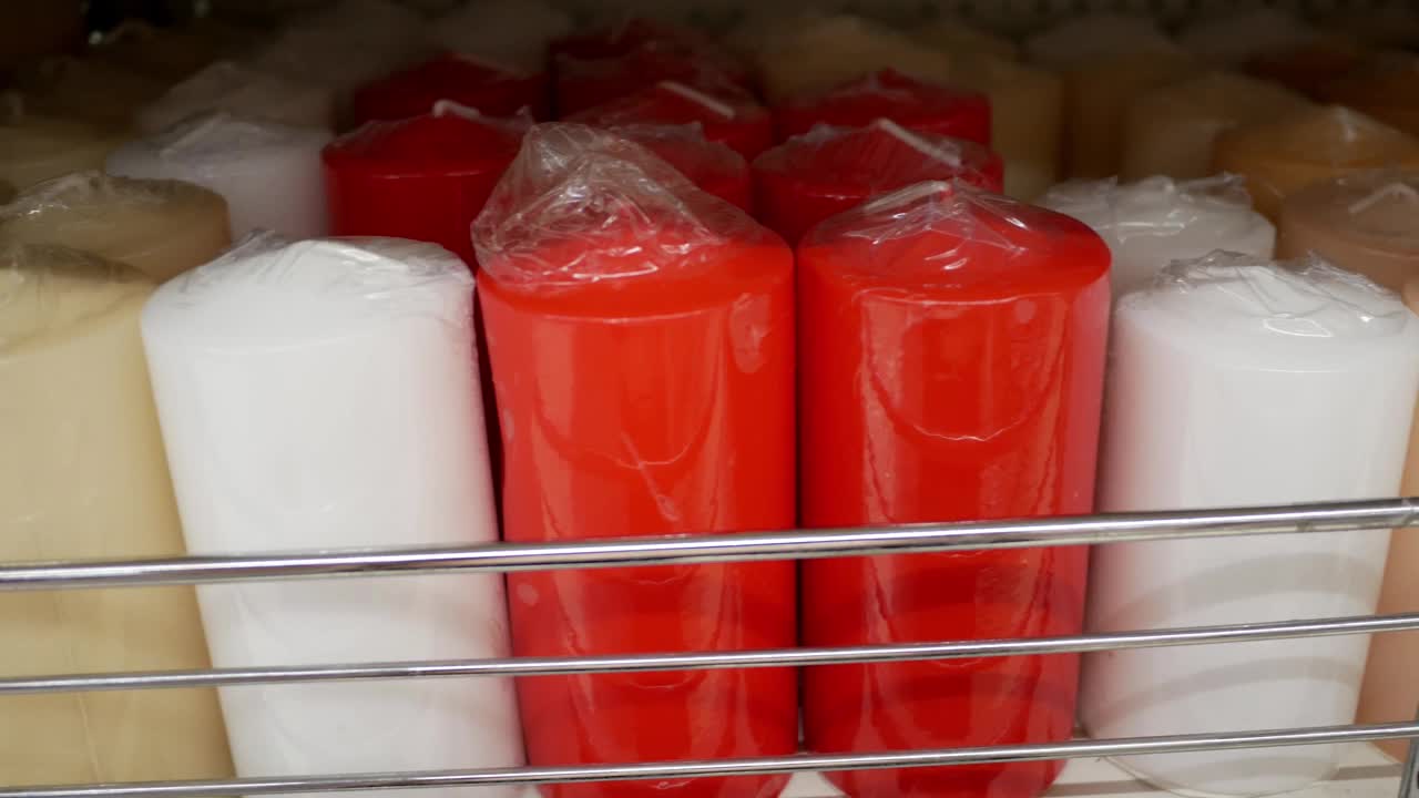 一个女人的手在一堆蜡烛中挑选一支红色的蜡烛。在商店或仓库包装的彩色蜡烛。制作和生产蜡烛。视频下载