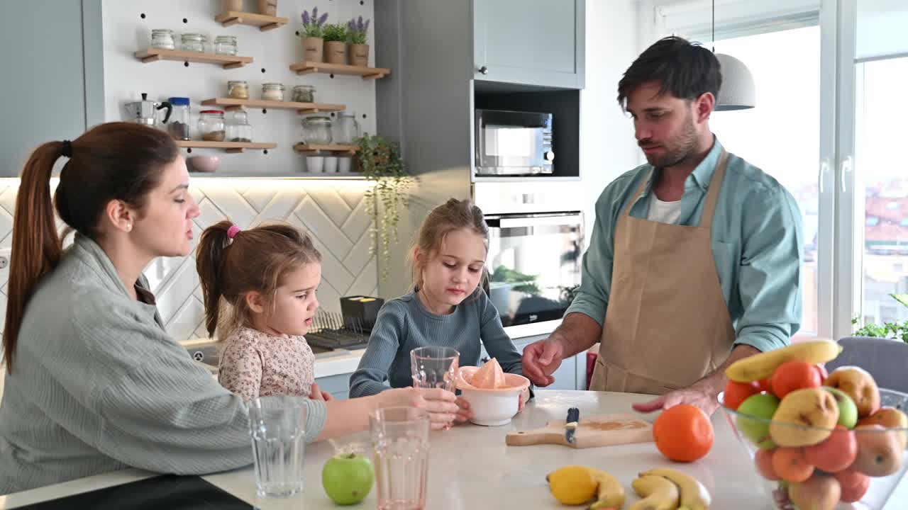 有孩子的家庭在家里准备健康的有机果汁。妈妈和爸爸在厨房里榨鲜榨果汁视频下载