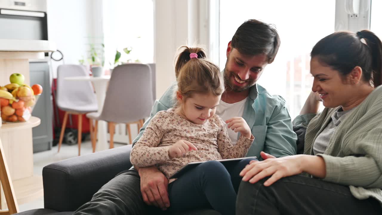 千禧一代的父亲和女儿坐在沙发上玩数码平板电脑视频下载