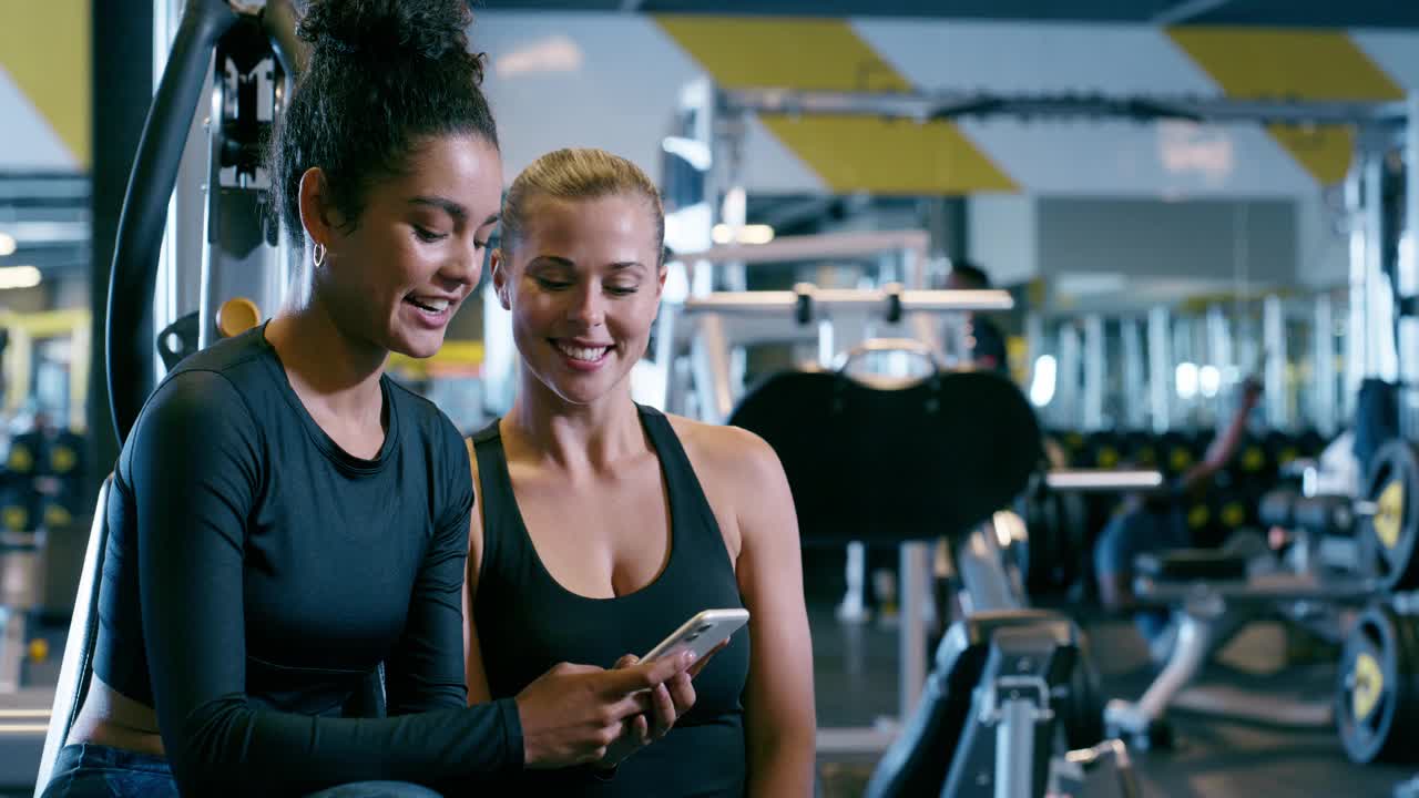 朋友，女人和笑声在健身房用智能手机，在社交媒体上锻炼后滚动或阅读健身博客。训练后放松一下，在网上看喜剧，用手机发表情包或有趣的聊天来增进感情视频下载