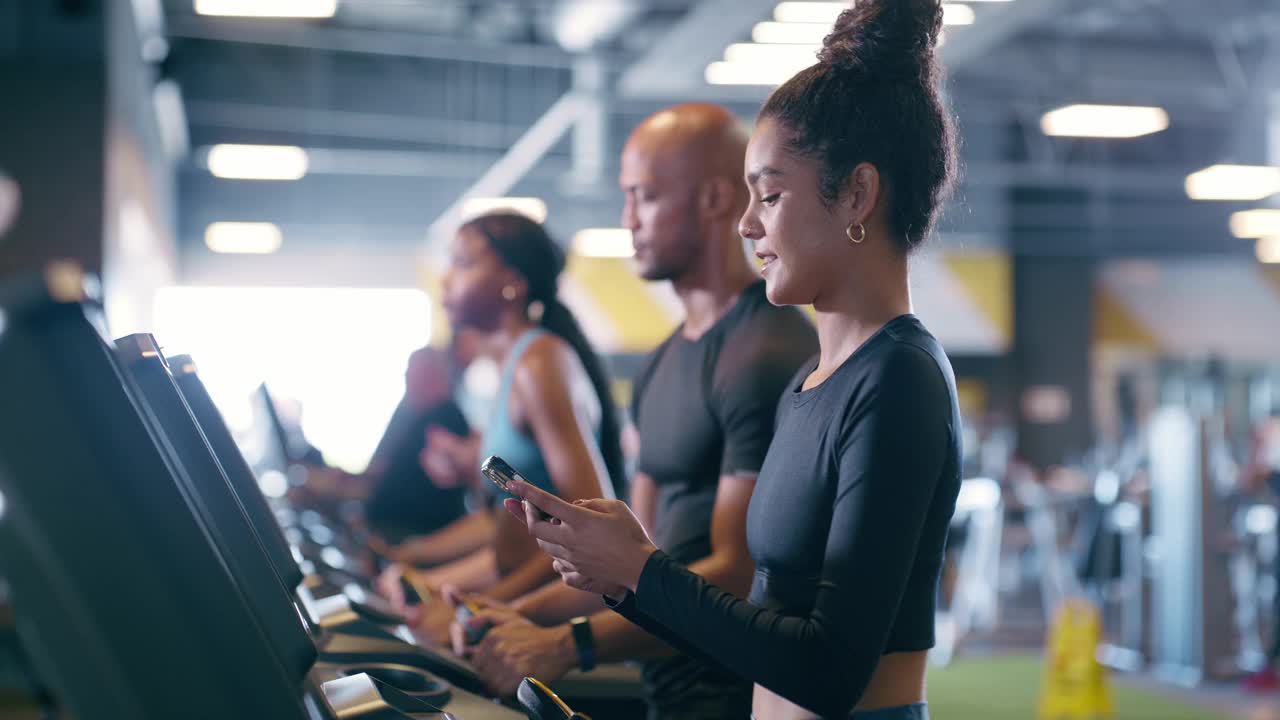 女人，用手机在健身房的跑步机上锻炼，一边锻炼一边发短信、手机聊天和打字。私人教练，运动员和训练与性能应用程序，有氧运动或快乐散步视频下载