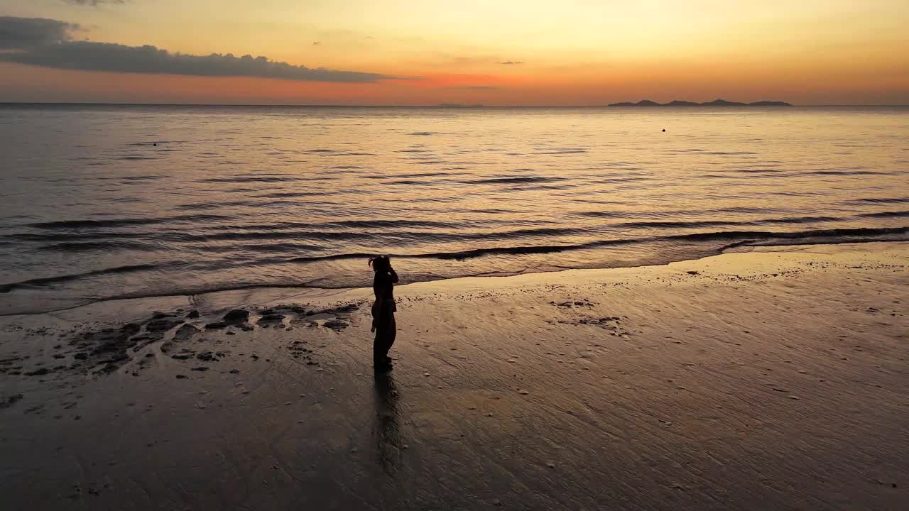 一个女人独自走在沙滩上，从空中看到夕阳视频下载