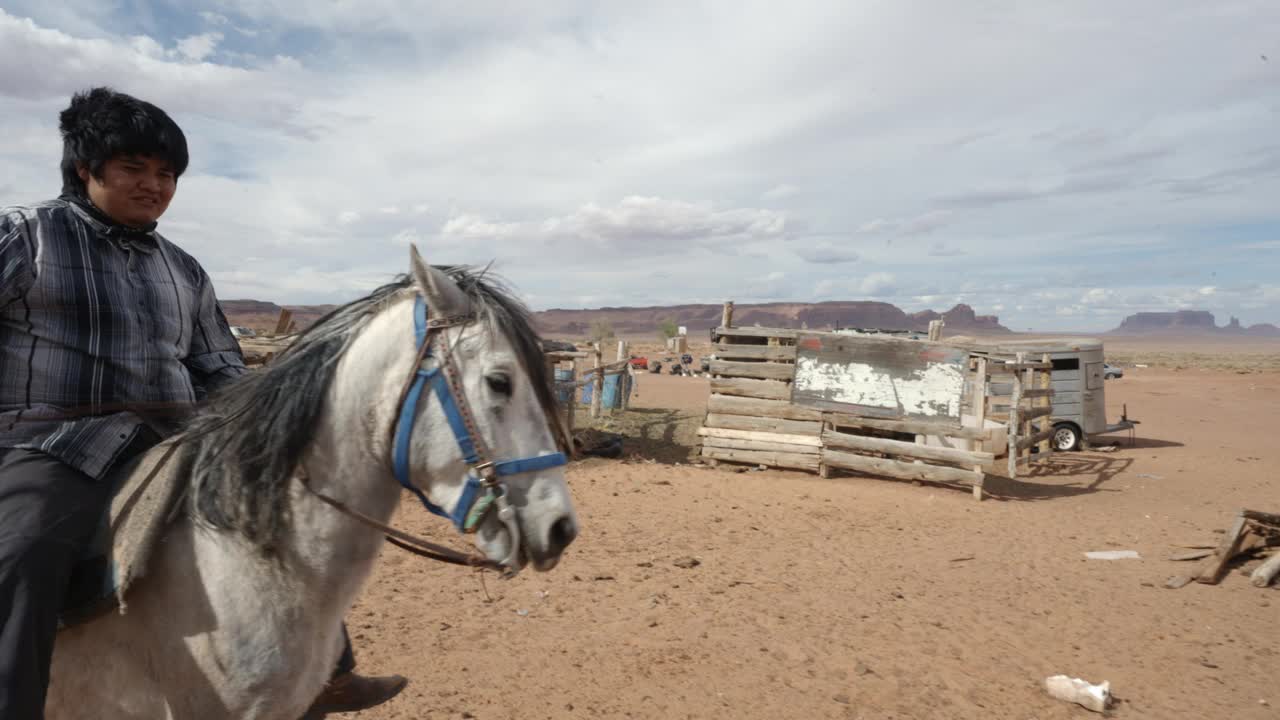 20多岁的年轻纳瓦霍人骑着他的马在纪念碑谷部落公园附近的家庭牧场在犹他州和亚利桑那州边境的沙漠视频下载