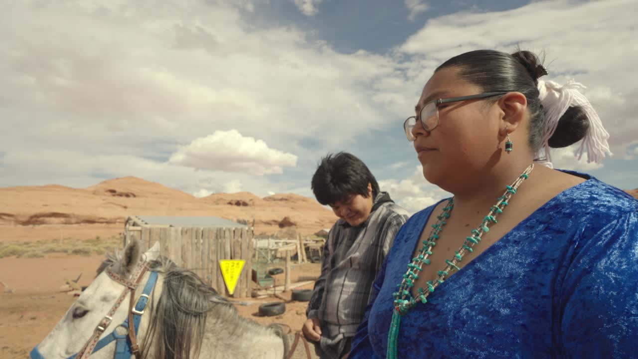 20多岁的年轻纳瓦霍夫妇在纪念碑谷部落公园的家庭牧场上骑马，背景是美丽的岩层视频下载