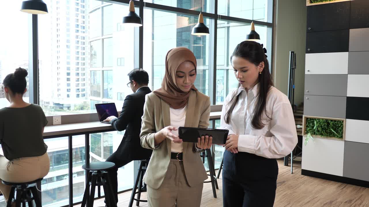 现代办公环境中多元化的商务人士，一起工作，共享信息。两位女企业家使用数码平板电脑视频下载