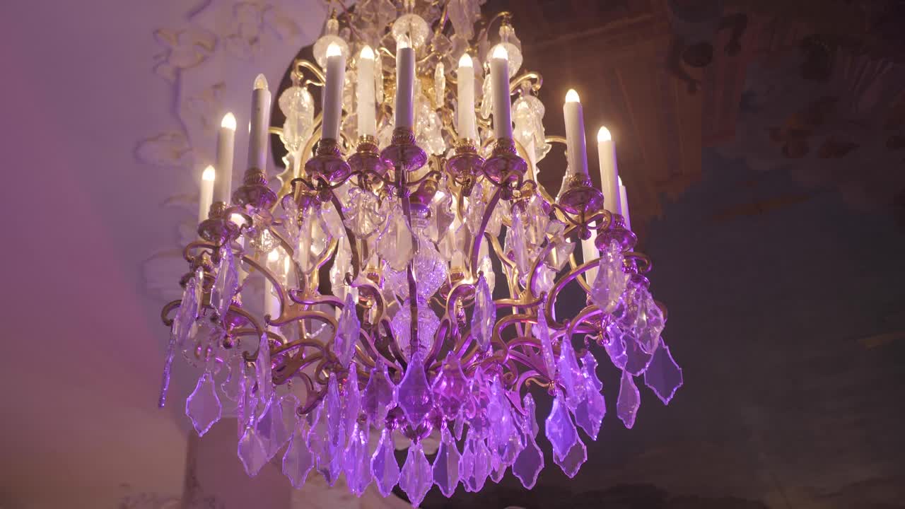 昂贵的大水晶吊灯高高挂在天花板上，漆成紫色。光线移动，特写镜头。视频下载