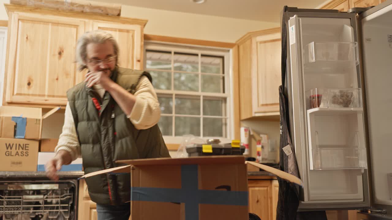 送货到家和新餐具:一个成熟的男人拿着新刀，在他的新房子里打开纸箱。视频下载