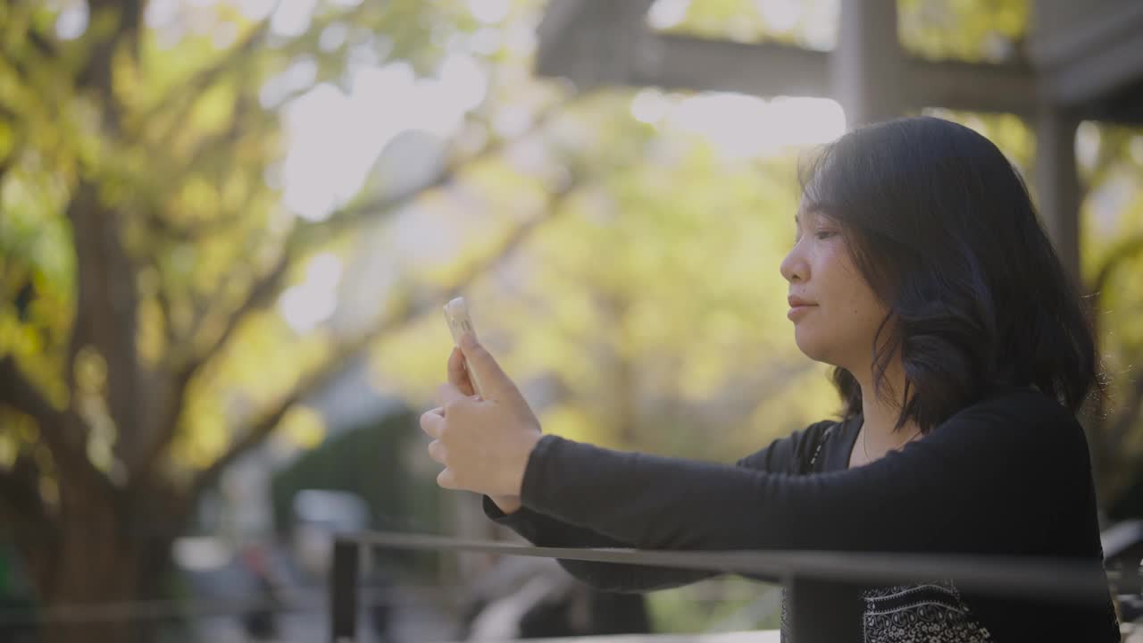 秋天，一名亚洲女子在城市公园用手机进行在线视频通话，并对着屏幕挥手。视频下载