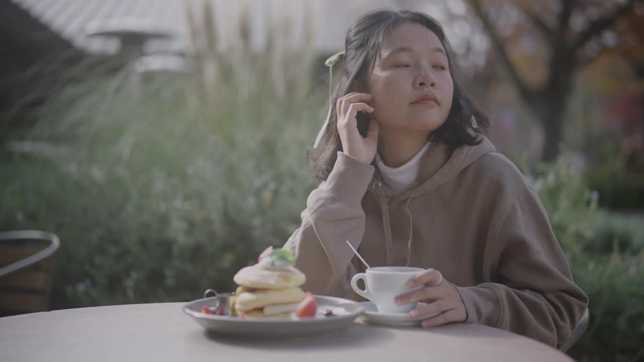 一个寒冷的秋天，年轻的亚洲女子在咖啡馆里放松。她在一个阳光明媚的日子里喝咖啡。视频下载