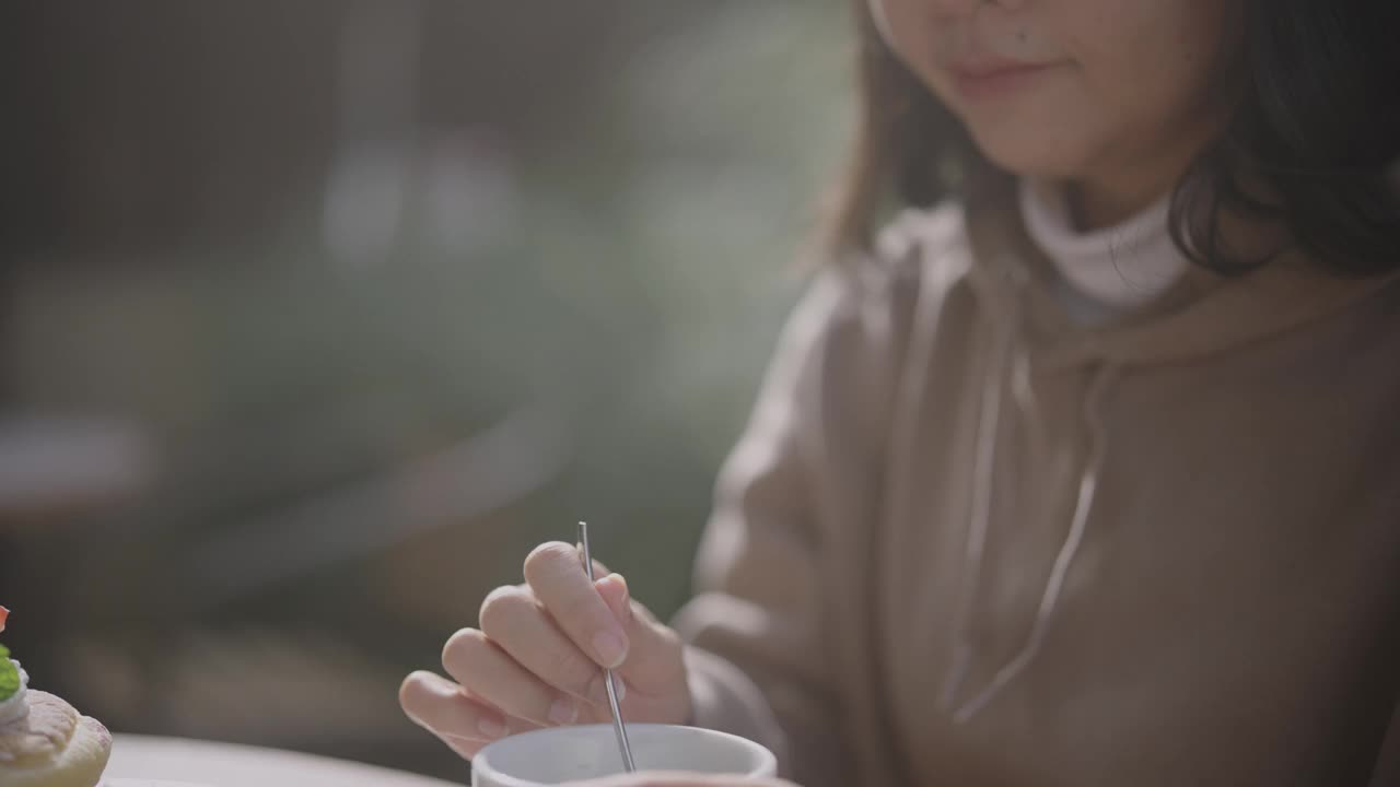 迷人的亚洲年轻女子在秋天的一个阳光明媚的日子里在咖啡馆喝咖啡。视频下载