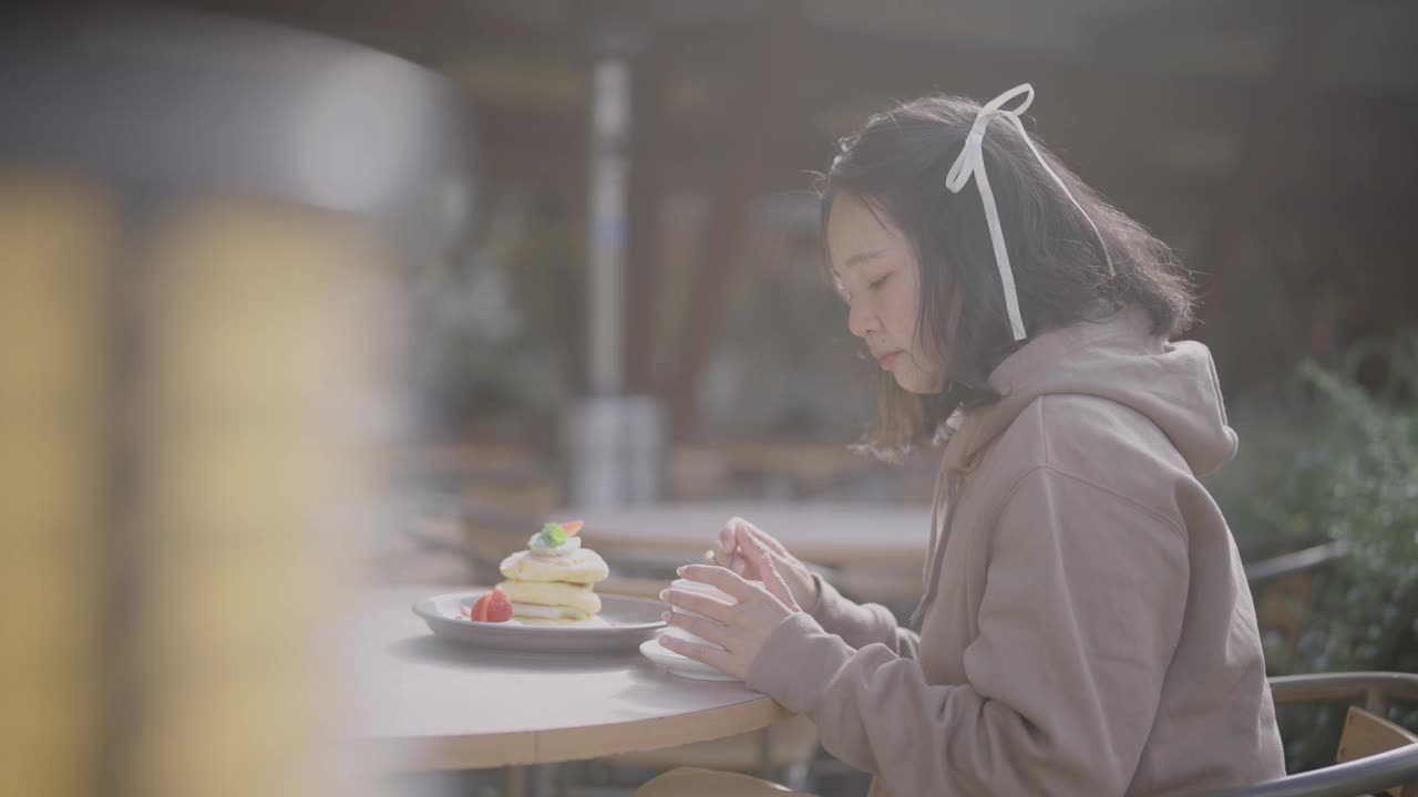 迷人的亚洲年轻女子在秋天的一个阳光明媚的日子里在咖啡馆吃煎饼。视频下载