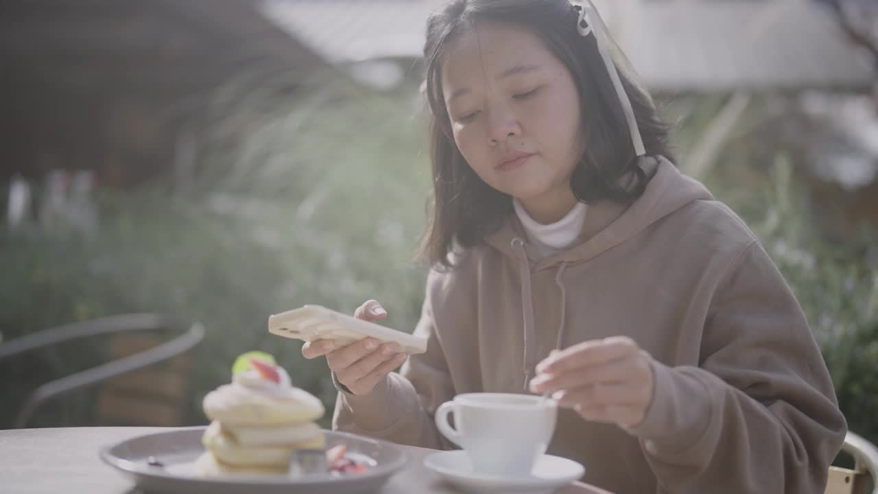 迷人的亚洲年轻女子在秋天的咖啡馆享受甜点。视频下载