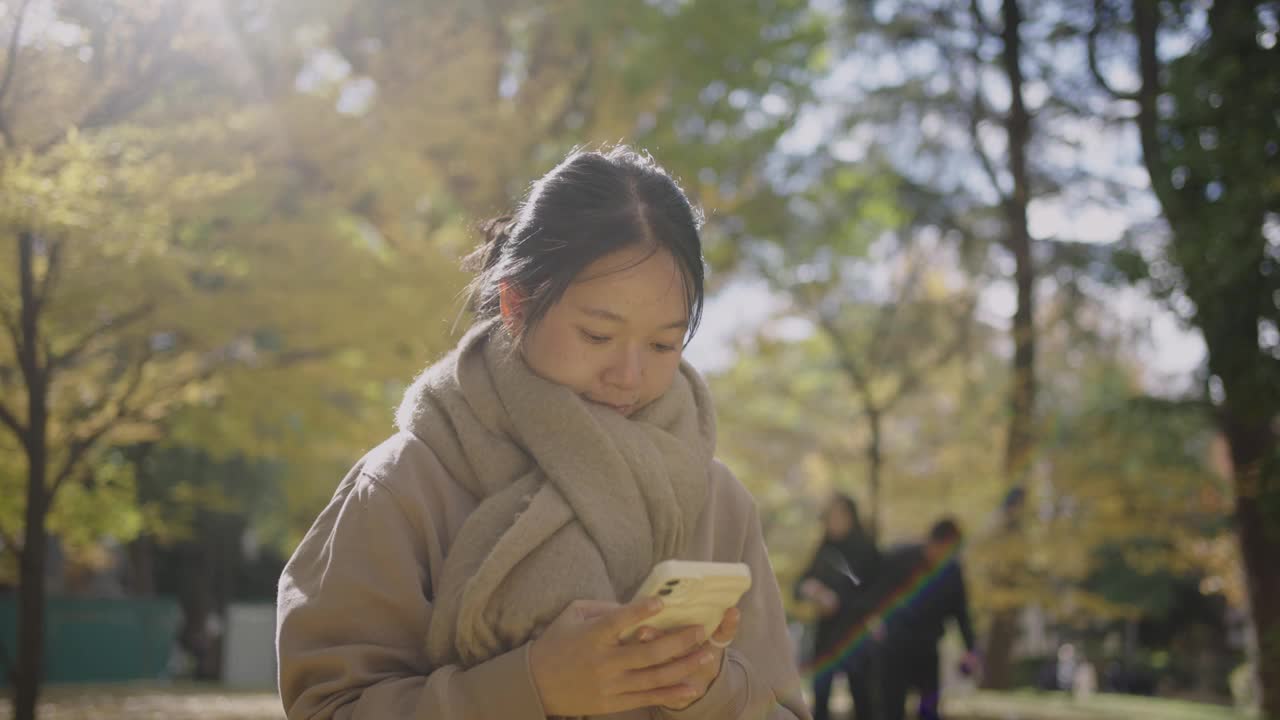 秋天，一名年轻女子在城市公园的视频通话中挥舞着智能手机，展示了令人惊叹的景色。视频下载