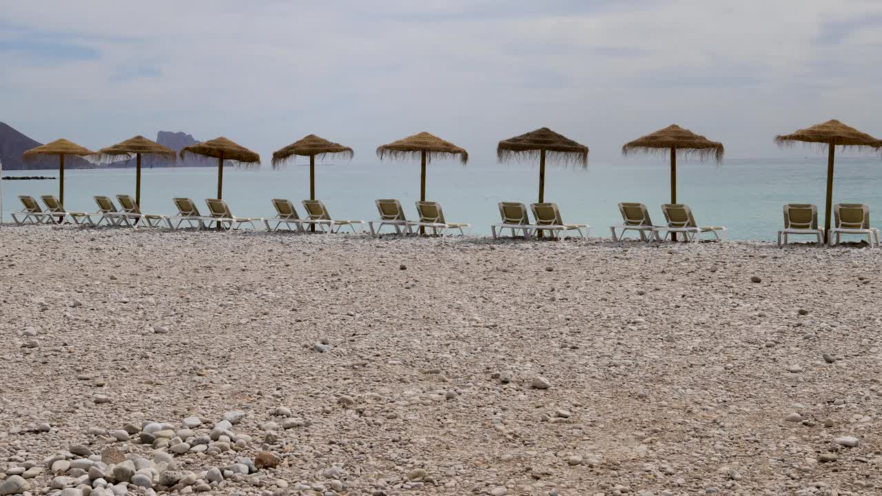 西班牙阿利坎特阿尔特亚美丽海滩的视频显示，沙滩上有日光浴躺椅和草编沙滩伞视频下载