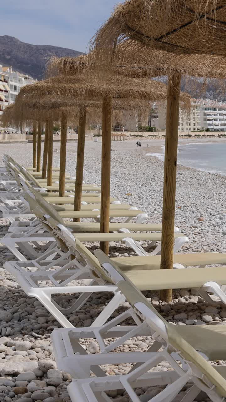 西班牙阿利坎特阿尔特亚美丽海滩的肖像镜头显示，沙滩上有日光浴躺椅和草编沙滩伞，沙滩被称为Playa La Roda视频下载