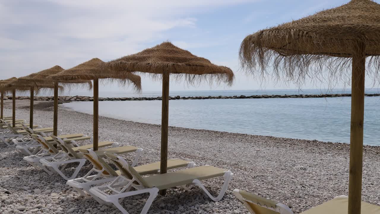 西班牙阿利坎特阿尔特亚美丽海滩的视频显示，沙滩上有日光浴躺椅和草编沙滩伞视频下载