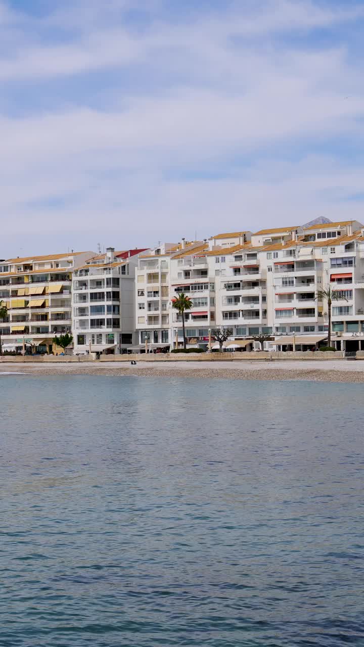 这是西班牙阿利坎特阿尔特亚美丽海滩的肖像镜头，展示了被称为Playa La Roda的卵石海滩前的酒店和餐馆视频下载
