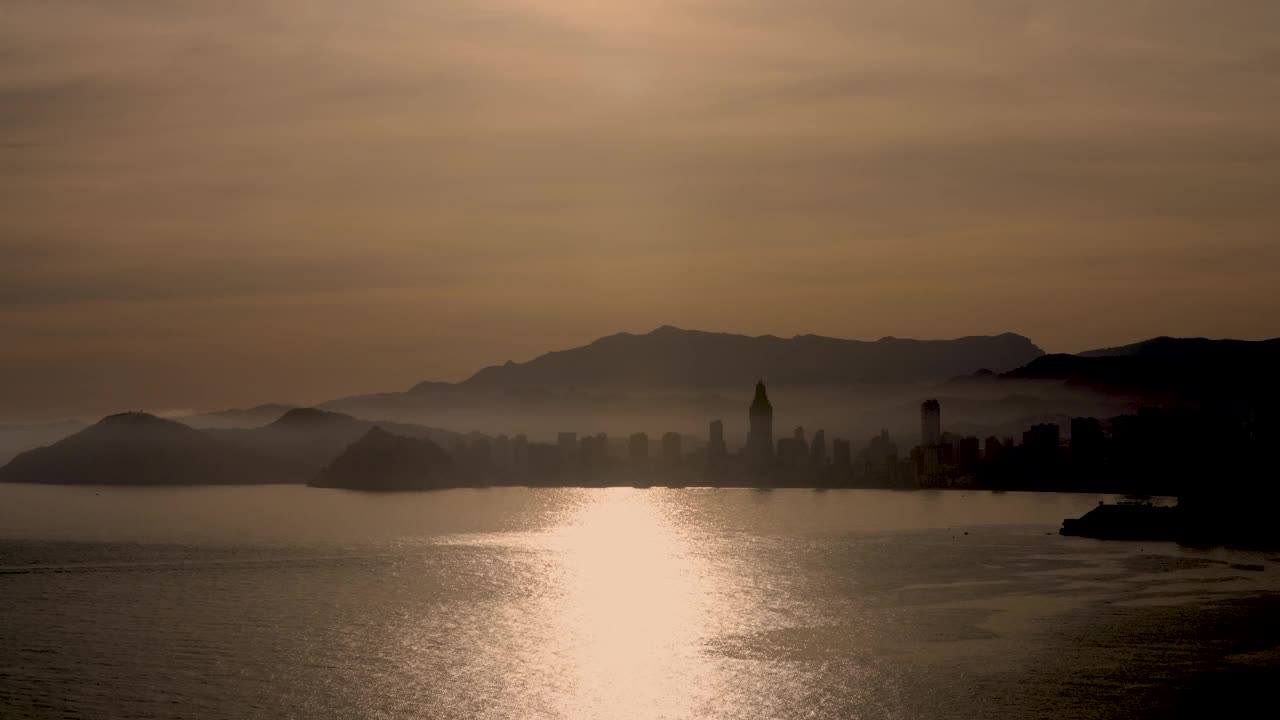 西班牙贝尼多姆镇夕阳西下的画面，背景是山脉和酒店的剪影视频下载