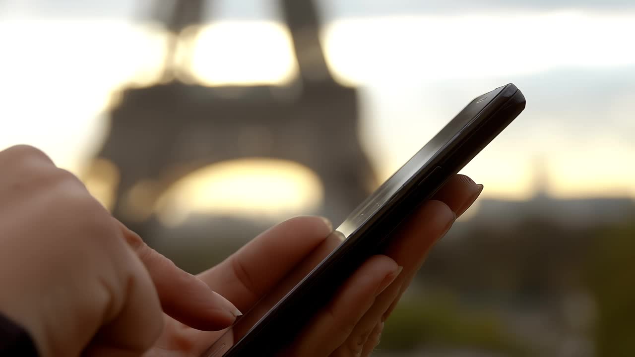 在埃菲尔铁塔的背景下，一个男孩的手触摸着智能手机视频下载