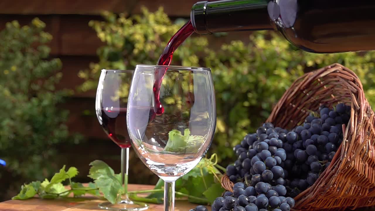 手把红酒倒进玻璃杯里，背景是深紫色的葡萄视频下载