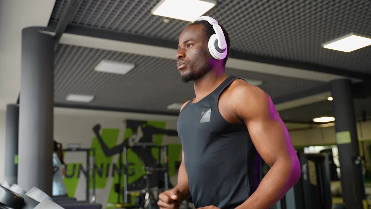 一个戴着耳机的男人在现代健身房的跑步机上跑步视频下载