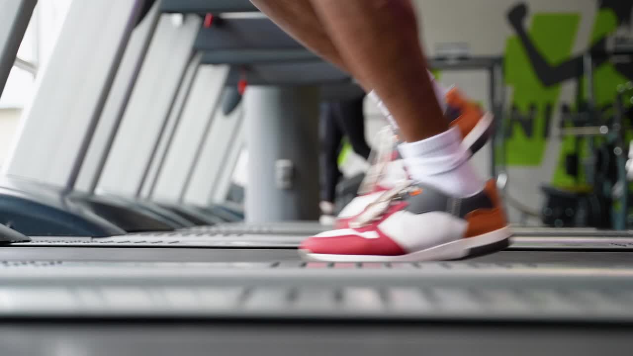 年轻的非裔美国人在健身房的跑步机上跑步，腿的特写视频下载