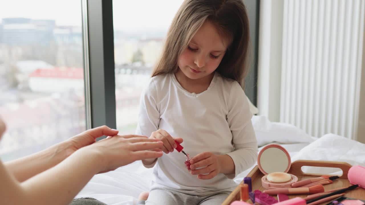 可爱的小女孩通过在妈妈手上涂指甲油来学习涂指甲。视频下载