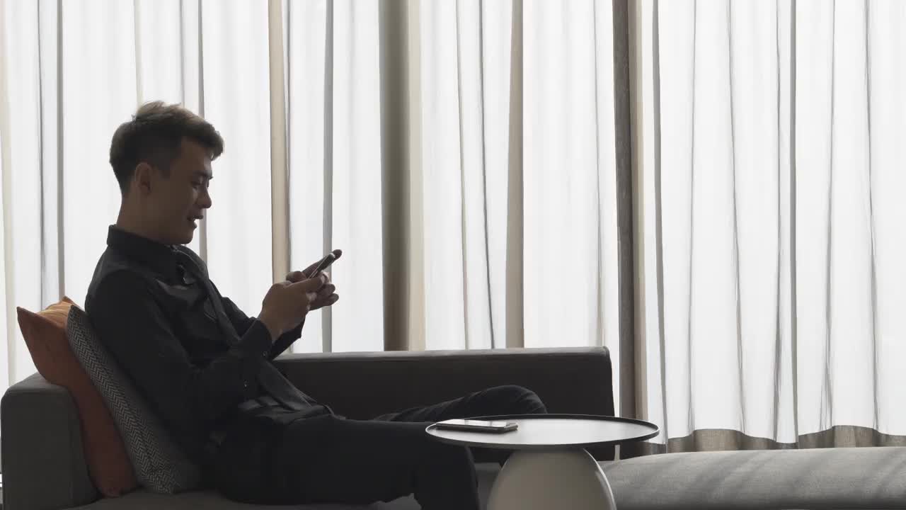 一个亚洲人在房间里玩手机视频下载
