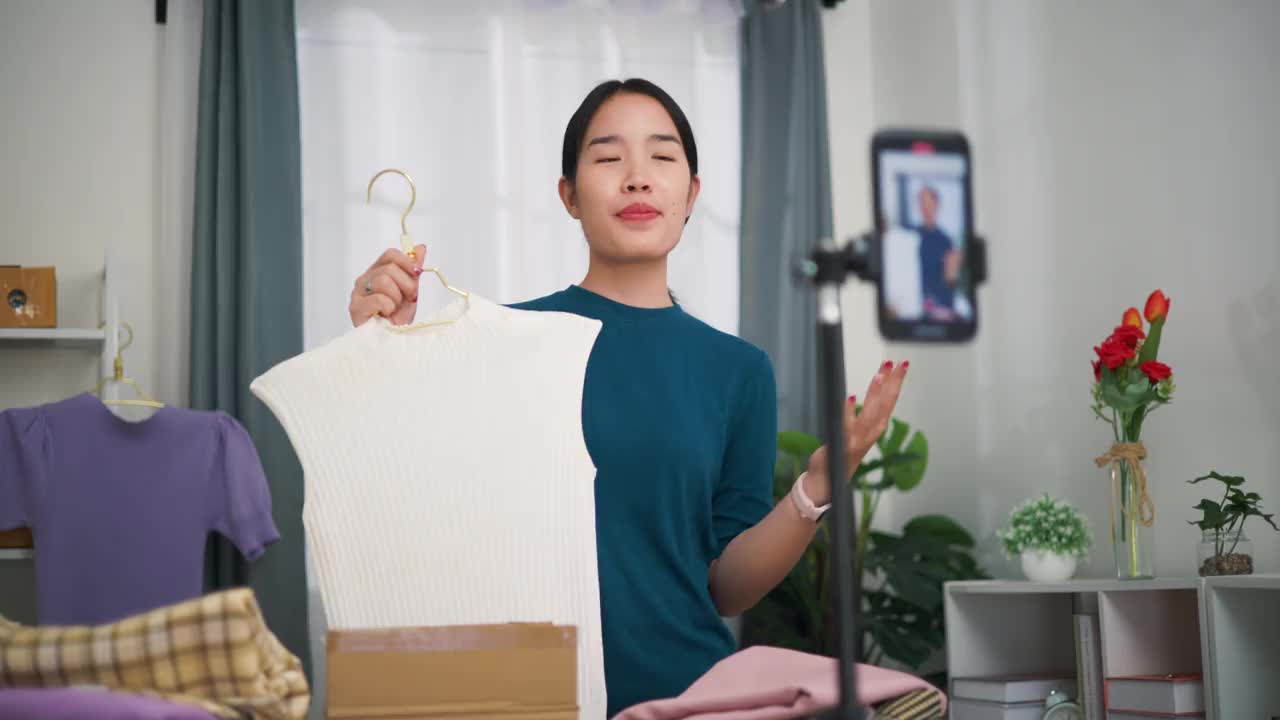 年轻的女企业主站在一边卖衣服，一边用手机直播，向顾客展示最新的时装系列。视频下载