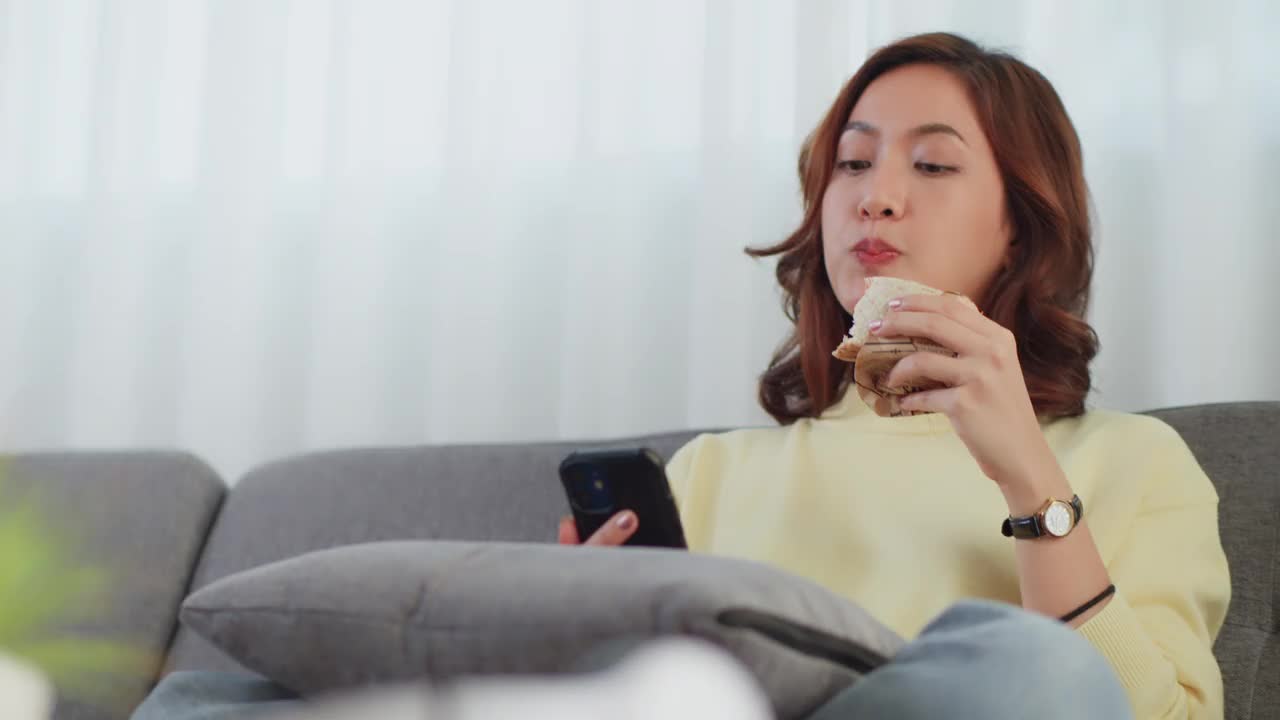 生活方式亚洲女人吃三明治拿着电话视频通话和自拍视频下载