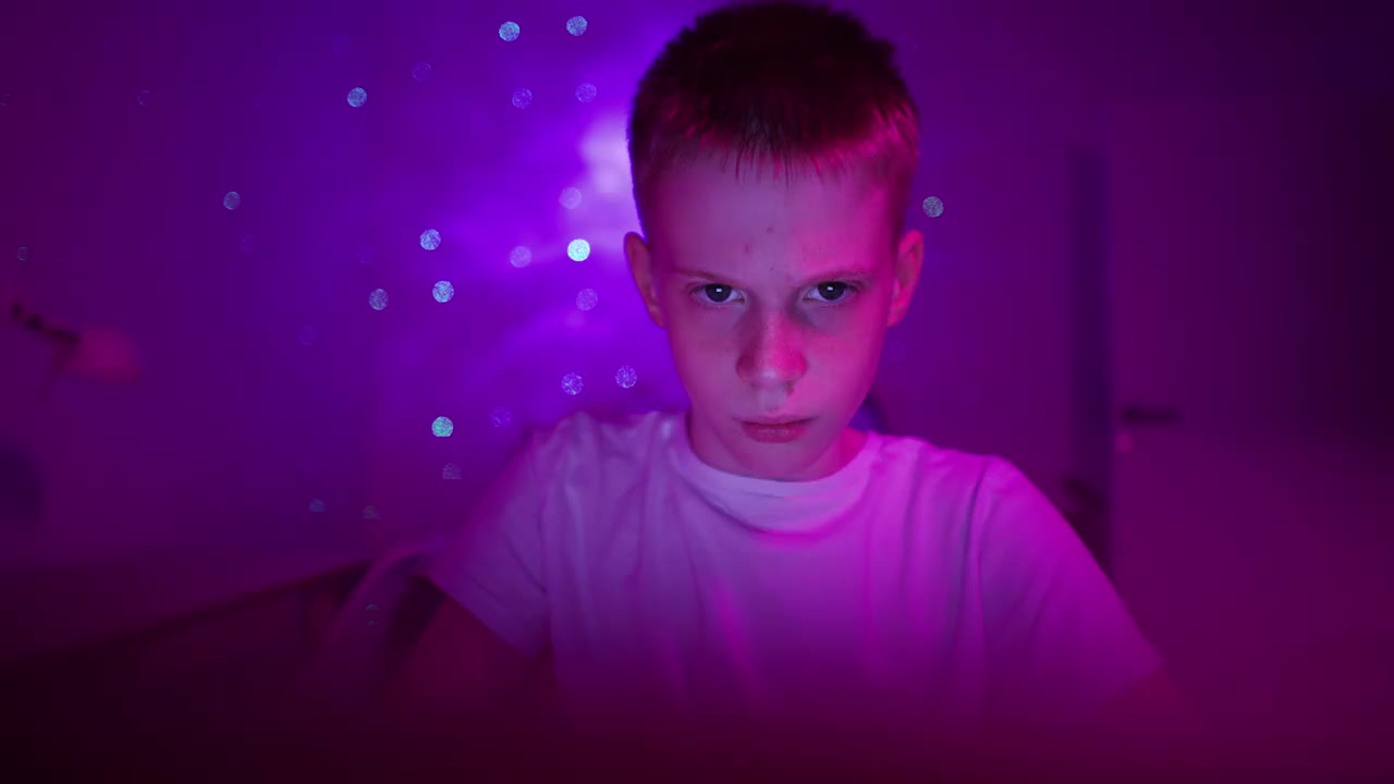 一个沉迷的白人男孩，在一间紫色灯光的房间里玩电子游戏视频下载